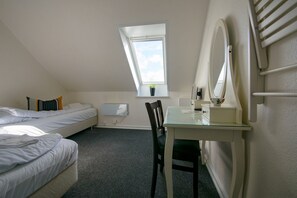 A small, tidy room with a bed, a desk, a chair, a mirror, and a window.