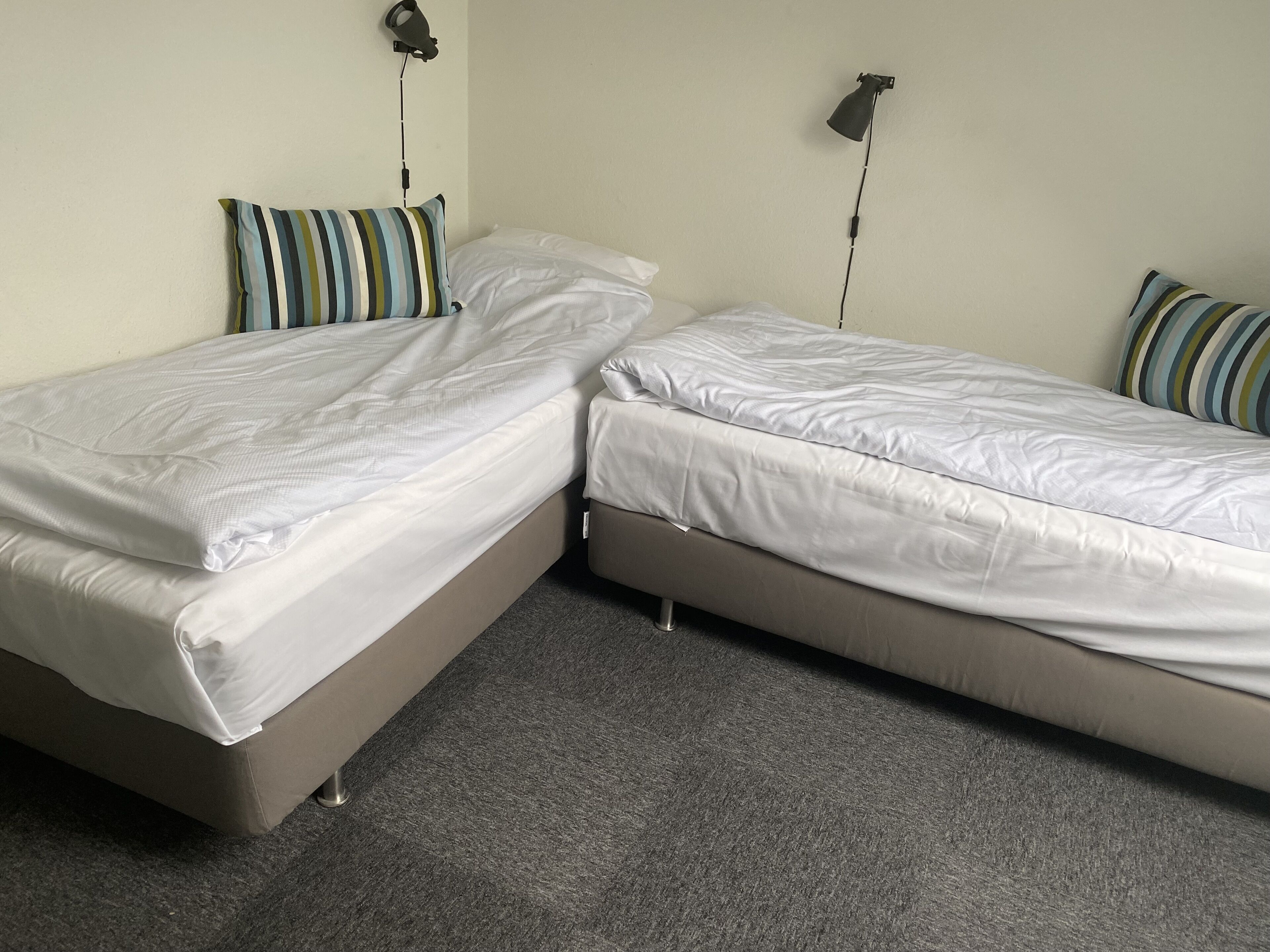 Et værelse med to enkeltsenge, hver med pude og lampe.