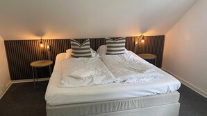 A neatly made bed with white linens and striped pillows, two bedside tables with lamps, and a sloped ceiling.