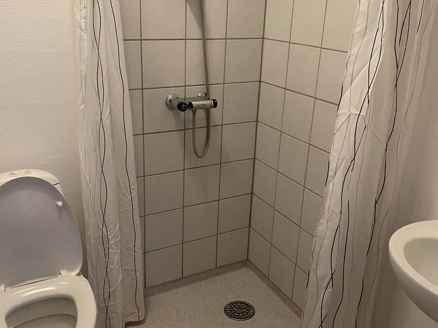 Un baño pequeño con azulejos, que incluye una ducha, inodoro y lavamanos.