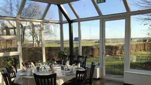 A dining area with a table set for six, large windows, and a view of the countryside.
