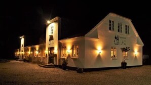 A white building with multiple windows and a central entrance, illuminated by exterior lights.