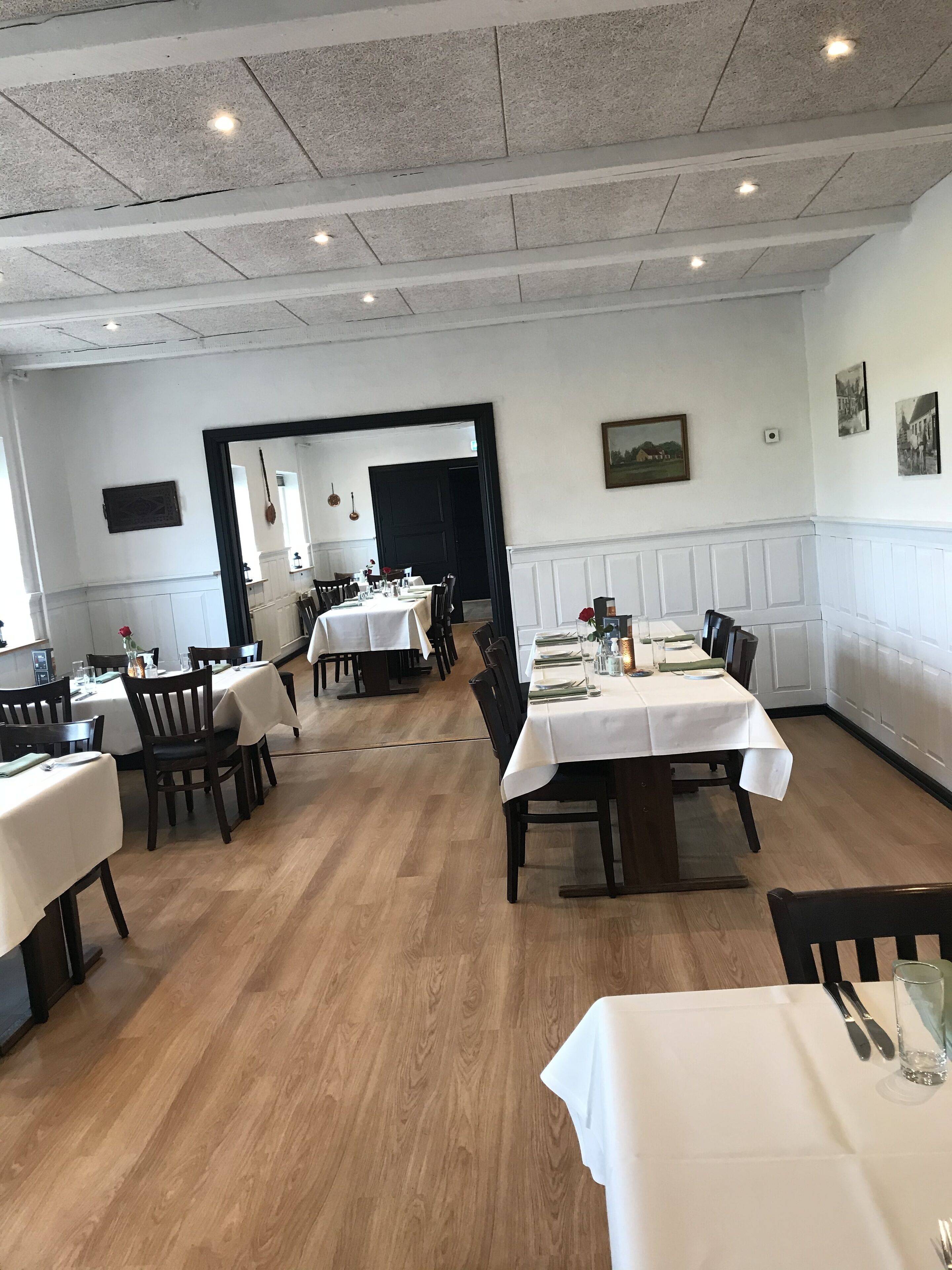 Interior de un restaurante con varias mesas y sillas, suelo de madera y un techo alto con iluminación empotrada.