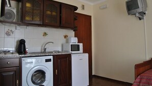 Een functionele keuken met een wasmachine, magnetron en kleine koelkast.