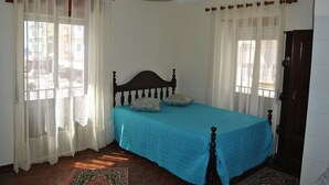 Een slaapkamer met een bed, gordijnen, een houten hoofdeinde, een deur en een vloerkleed met een patroon.