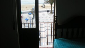 Een kamer met balkon dat uitkijkt op een strand, met een bed en uitzicht op zee.