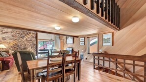A wooden dining area with a high ceiling and exposed beams, a stone wall, and a staircase with a wooden railing. - Snowcreek 91: Nice, Dog Friendly, Close to Red Lin (Mammoth Lakes)
