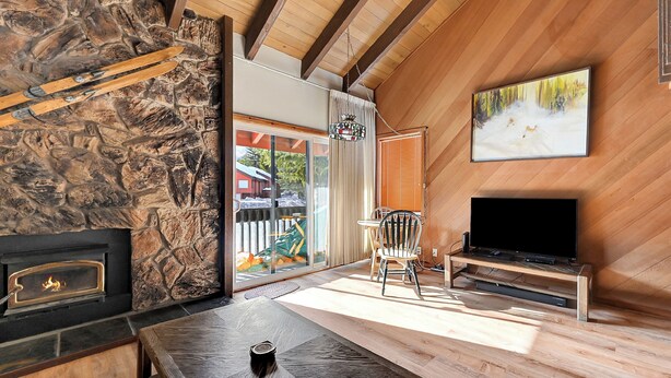 A cozy room with a stone fireplace, wooden ceiling beams, a television on a wooden stand, and a painting on the wall. - Snowcreek 91: Nice, Dog Friendly, Close to Red Lin (Mammoth Lakes)
