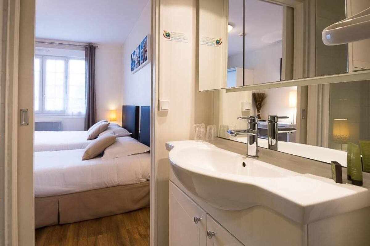 A hotel room with a bed, a large mirror, a sink, and a window with curtains.