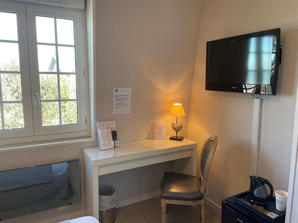 Ein Zimmer mit Schreibtisch, Stuhl, Fernseher, Lampe und einer Kaffeemaschine.