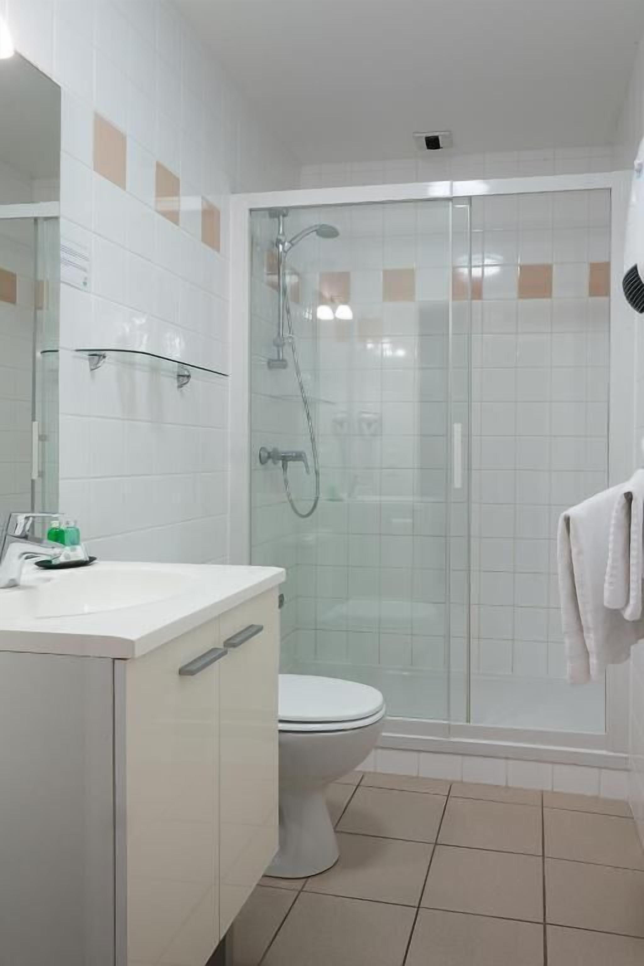 A bathroom with a glass-enclosed shower, a white toilet, and a white sink with a mirror.