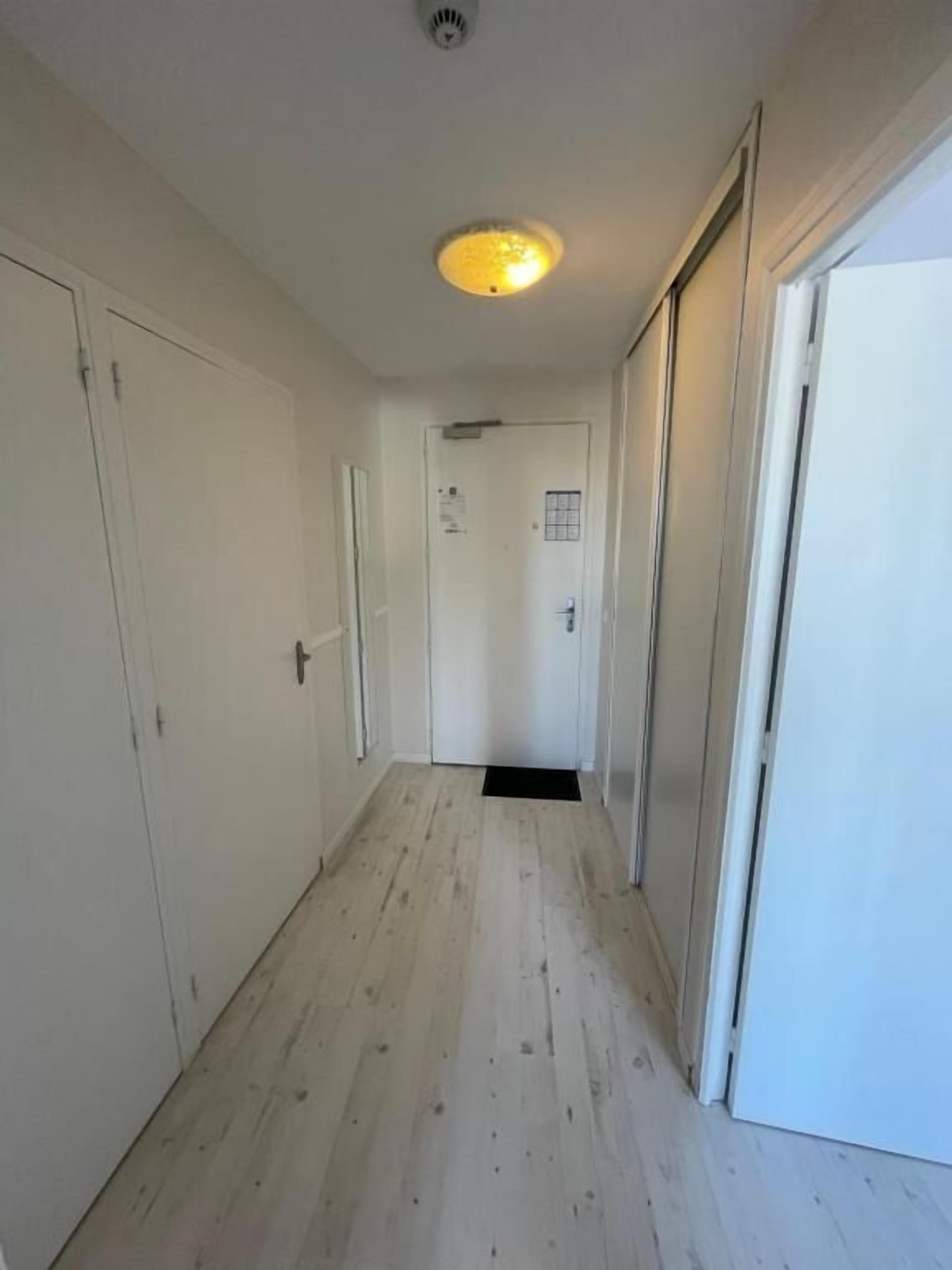 A narrow hallway with wooden flooring, white doors, and a ceiling light fixture.