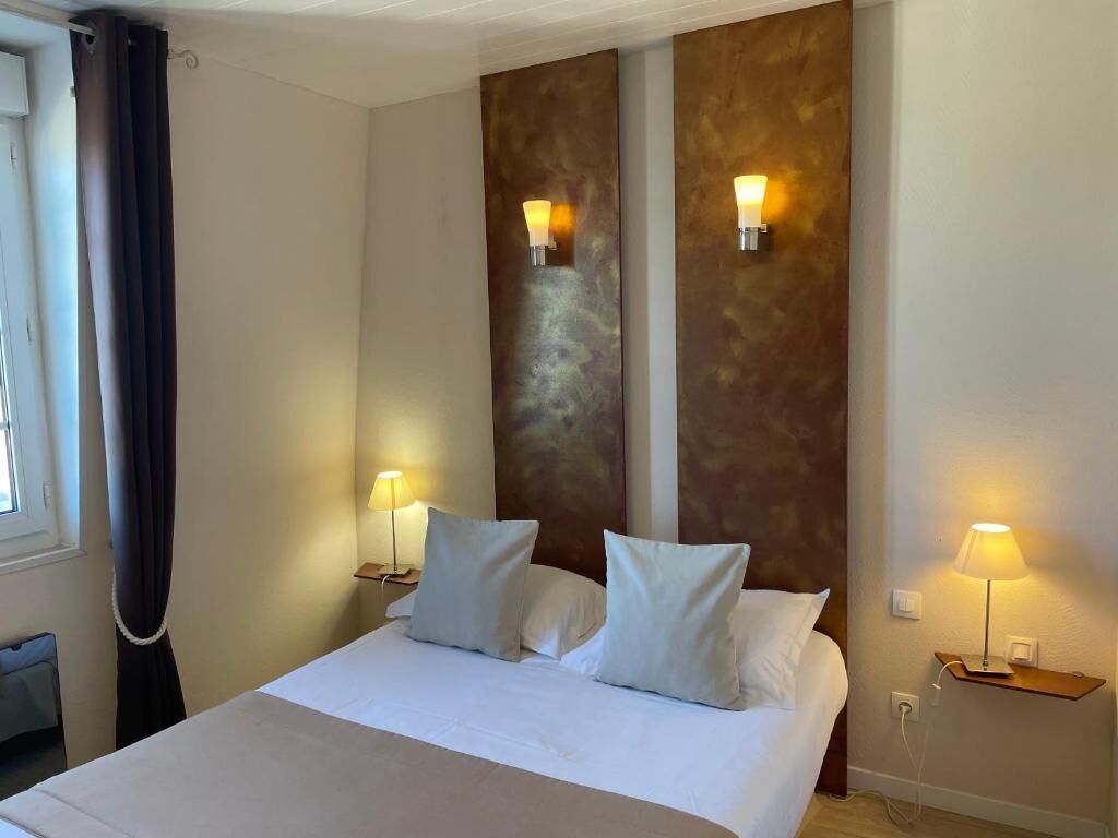 A hotel room with a large bed, two wall-mounted lamps, and a window with curtains.