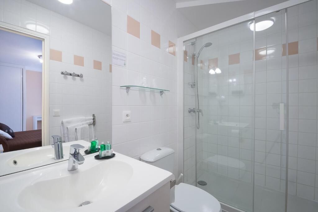 Une salle de bain avec un lavabo blanc, un miroir et une cabine de douche en verre.