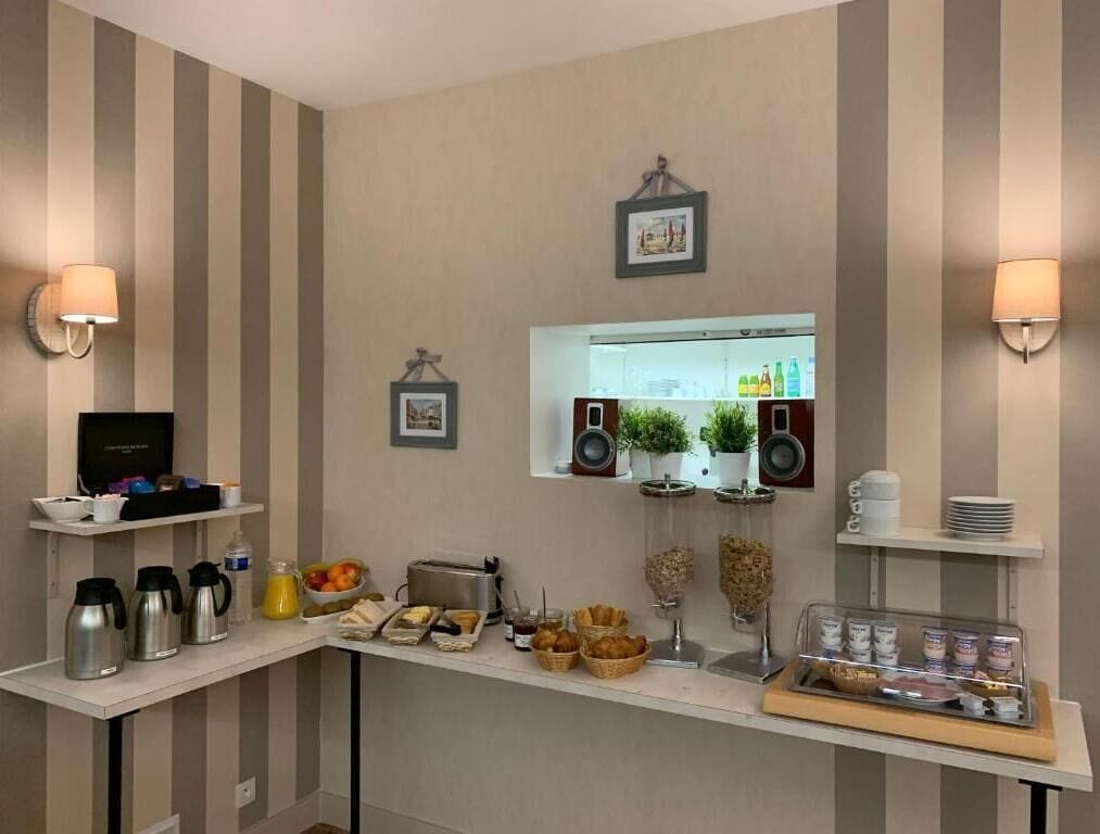 A breakfast bar with coffee makers, fruit, and pastries. There are wall-mounted speakers and a framed picture above the bar.