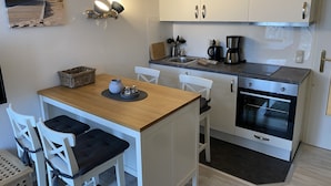 Eine kleine Küche mit weißen Schränken, einem Holztisch, zwei weißen Stühlen, einer Kaffeemaschine und einem eingebauten Backofen.