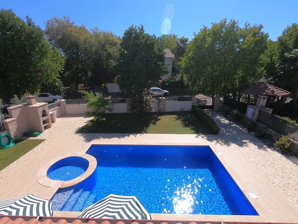 Une piscine avec un jacuzzi, entourée d’un jardin et agrémentée d’un petit kiosque.