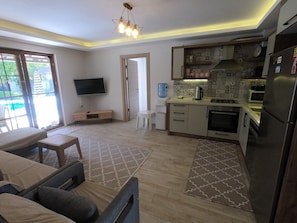 Une cuisine moderne équipée d’un four, d’un micro-ondes et d’un réfrigérateur encastrés. On y trouve également un coin repas avec une table et des chaises, ainsi qu’un téléviseur fixé au mur.