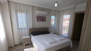 A bedroom with a large bed, a nightstand, a wall-mounted air conditioner, and a window with sheer curtains. - NEW LISTING! BEAUTIFUL 4 BEDROOM ALL EN-SUITE VILLA IN GULPINAR AREA OF DALYAN!! (Dalyan)