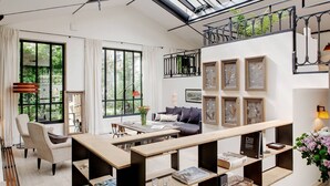 Amplia sala de estar con techo alto, ventanas grandes, una mesa de centro de madera, un sofá y una estantería.
