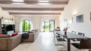 A spacious living area with a large sofa, a dining table with chairs, a TV, and a bookshelf.