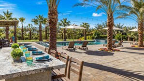 An outdoor dining area with a long table set for a meal, surrounded by palm trees and a pool. - SDR Hideaway! Misters, Saltwater Pool/Spa, Putt Putt! (Thousand Palms)