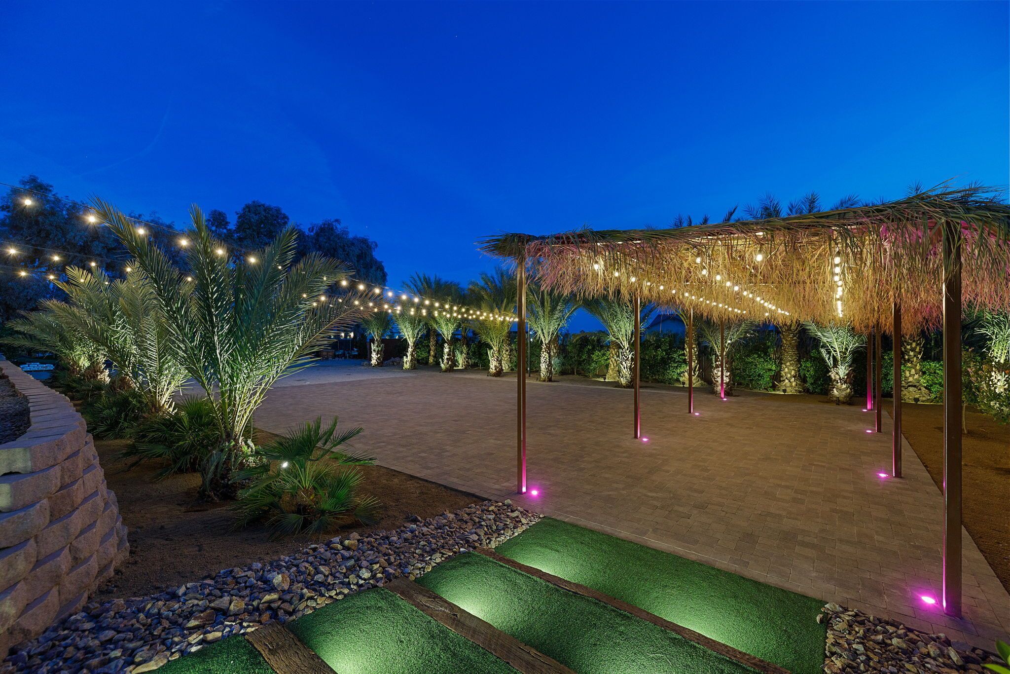 An outdoor area with a pergola, string lights, and artificial grass.