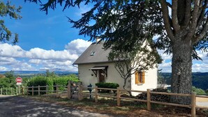 Une maison de campagne, avec un mur en pierre, une clôture en bois et une vue sur les montagnes en arrière-plan.