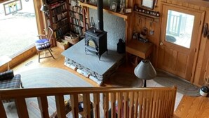 Ein gemütliches Blockhaus mit Kamin aus Stein, Holzregalen, einer Bücherwand und einer komfortablen Sitzecke.