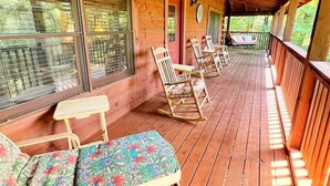 A covered wooden deck with rocking chairs and a bench, large windows, and a view of the outdoors. - Gem in the Glades, secluded, minutes from Gatlinbu (Gatlinburg)