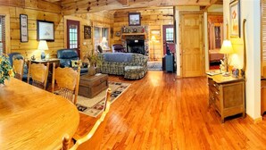 A cozy log cabin interior with a dining area, a living room with a fireplace, and a hallway leading to another room. - Gem in the Glades, secluded, minutes from Gatlinbu (Gatlinburg)