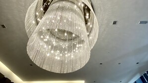 Un intérieur moderne agrémenté d’un grand lustre circulaire et d’une colonne centrale ornée d’une plante.