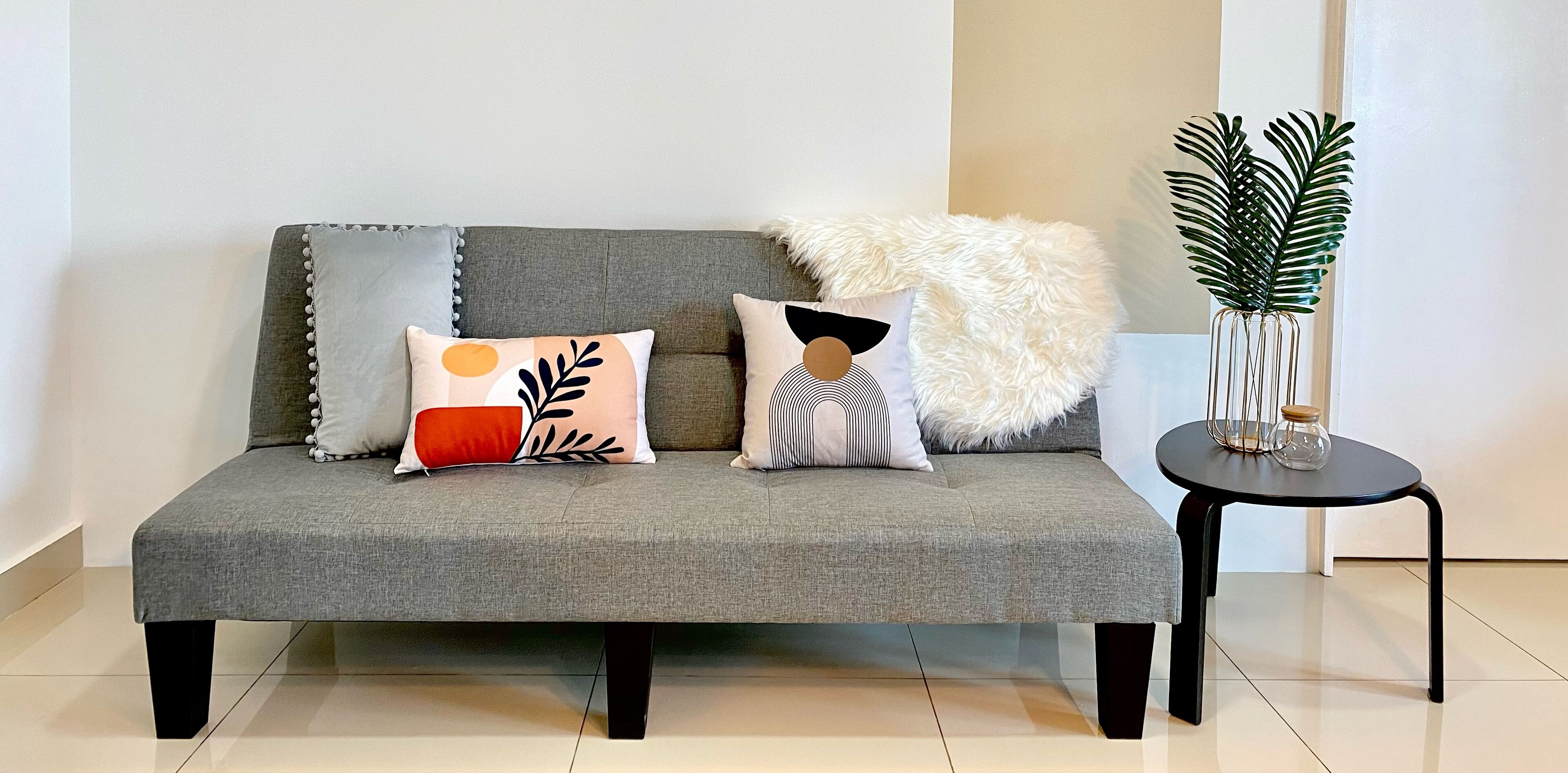 Ein graues Sofa mit dekorativen Kissen, einer flauschigen weißen Decke und einem kleinen schwarzen Tisch mit einer Pflanze.
