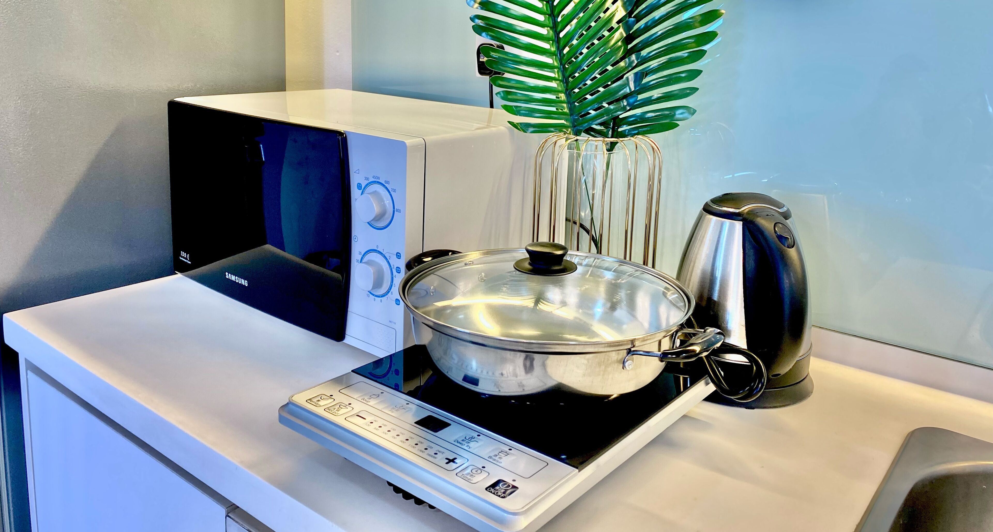 A kitchen with a microwave, a kettle, and a pot on an induction cooktop.