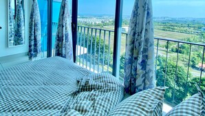 Une chambre avec un grand lit, des rideaux à motifs floraux et un balcon offrant une vue sur la ville.