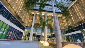 Un bâtiment moderne doté d’une façade en verre, de palmiers et de colonnes illuminées.