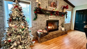 Een gezellige woonkamer met een grote kerstboom, een open haard en feestelijke decoraties.