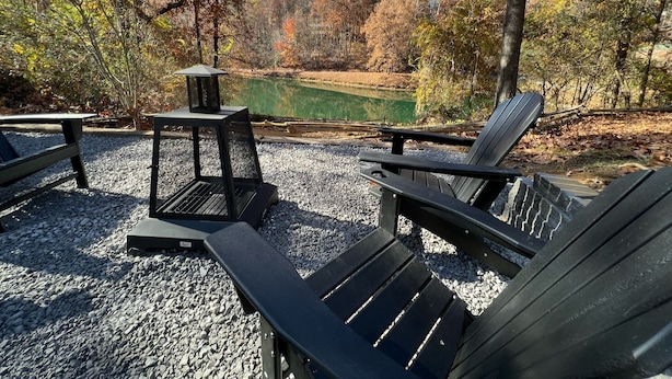 Een prieeltje met een tafel en stoelen in een park met een vijver en herfstbomen.