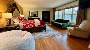 Een ruime slaapkamer met een groot bed, een groene bank, een beige fauteuil en een houten vloer.