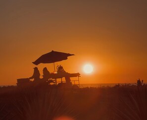 Escena de atardecer con la silueta de una silla de playa y una sombrilla contra el cielo.