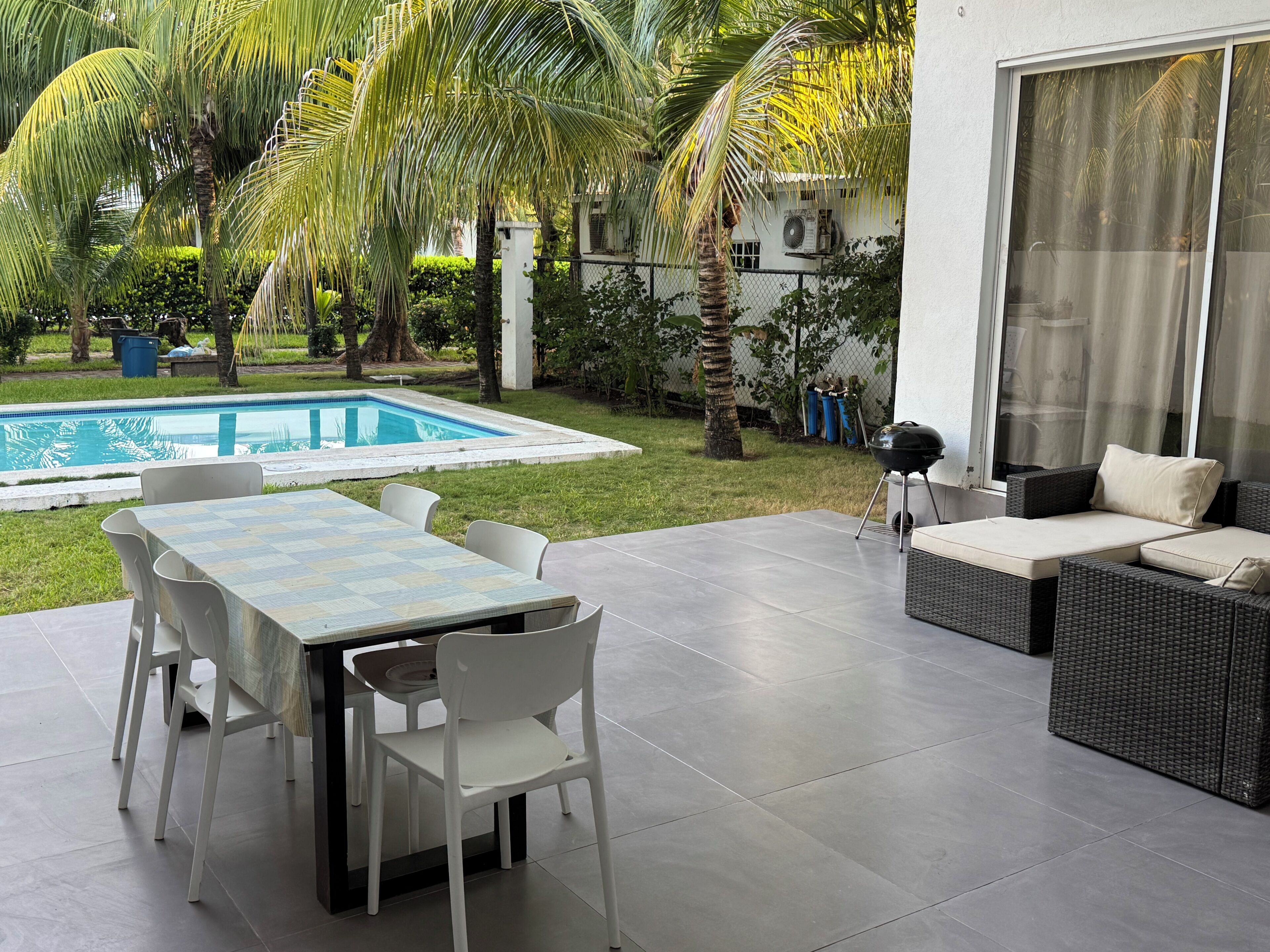 Un patio exterior con piscina, una mesa de comedor con sillas y un área de descanso con cojines.