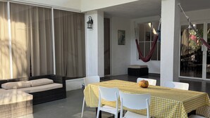 Un espace patio avec une table dressée pour deux personnes, des chaises blanches, un banc rembourré et un hamac.