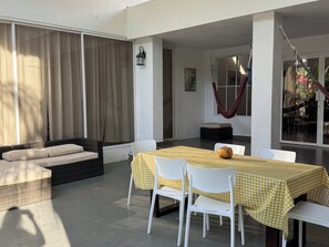 Un patio con una mesa dispuesta para dos, sillas blancas, un banco acolchado y una hamaca.