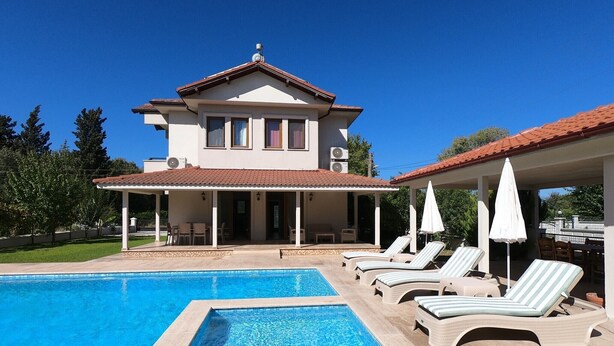 Ein zweistöckiges Haus mit Swimmingpool, Liegestühlen und einer überdachten Terrasse.