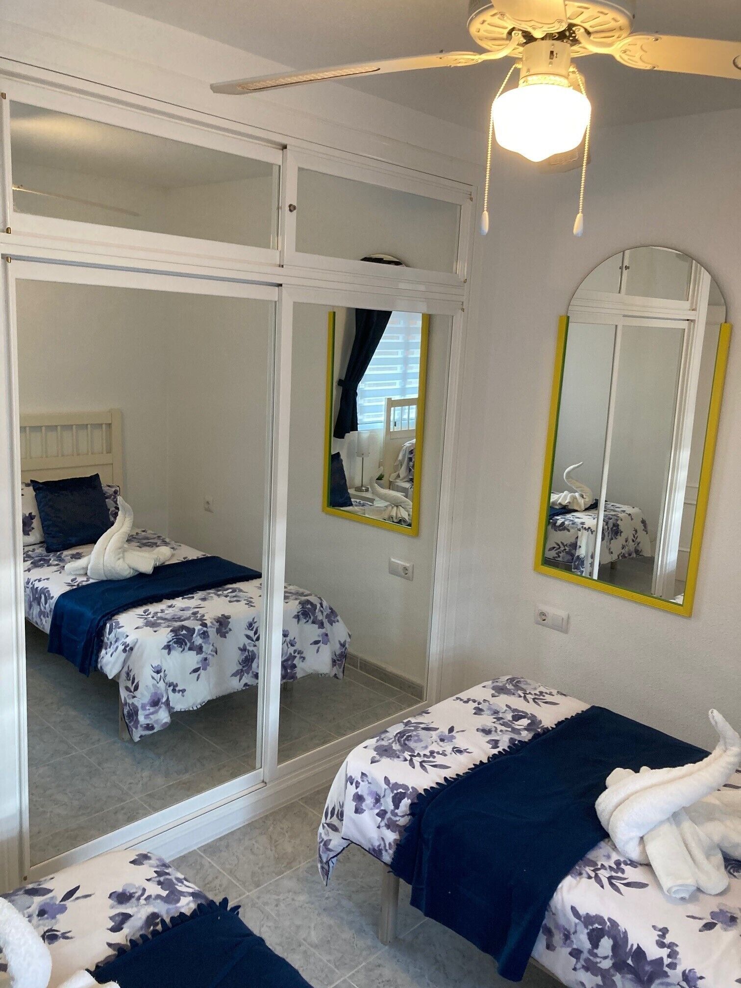 Een hotelkamer met twee bedden, een plafondventilator, een grote spiegel en uitzicht door een schuifdeur.