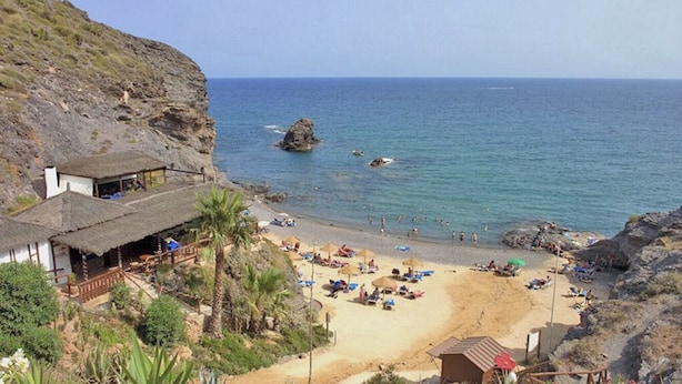 A beach with a thatched-roof building, a sandy shore, and rocky outcrops.