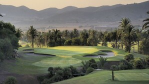 A golf course with sand bunkers, palm trees, and distant mountains.