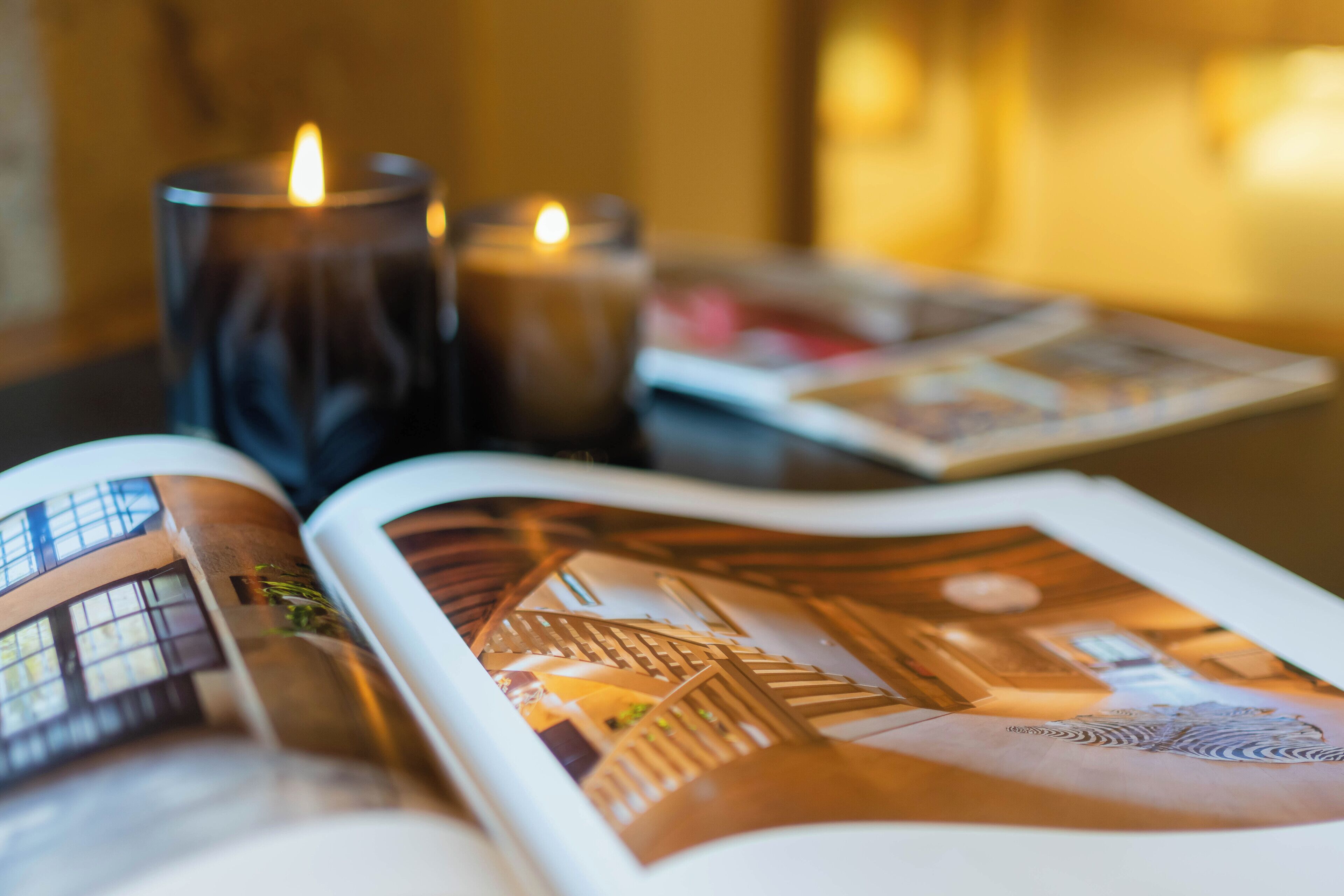 Una revista abierta que muestra la distribución interior de un edificio, dos velas y un libro sobre una mesa.
