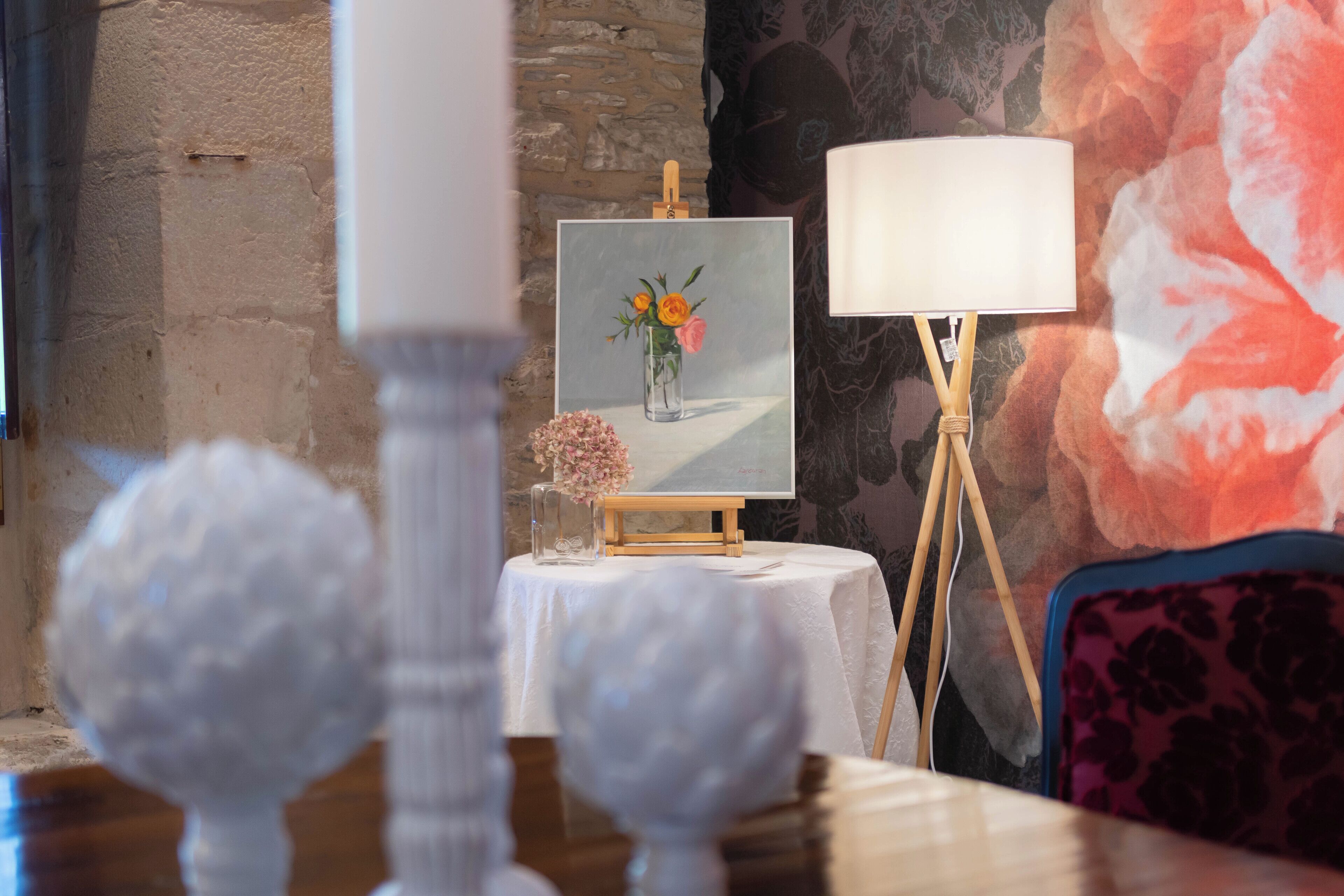 A room with a table displaying a framed painting of flowers, a lamp, and decorative items.