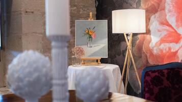 A room with a table displaying a framed painting of flowers, a lamp, and decorative items.